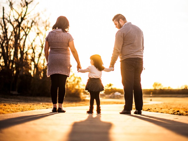 Fotografia de uma família de três pessoas caminhando ao por do sol.