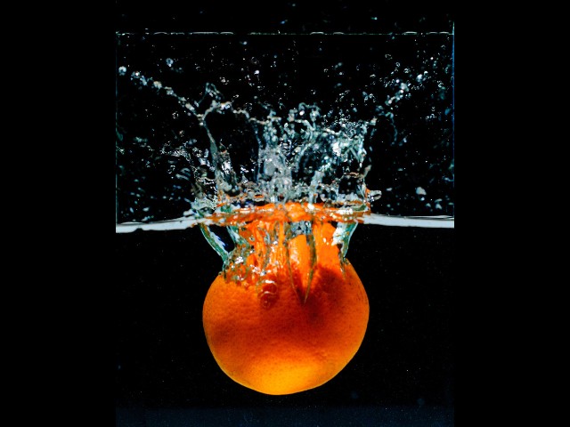 fotografia que capturou o movimento que aconteceu quando uma laranja é jogada em um recipeinte com água gerando um efeito interessante