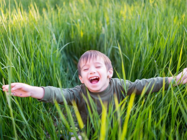 ensaio infantil criança sorrindo em um campo com folhagens verdes