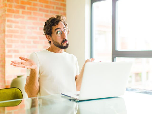 Homem com cara de dúvida e engraçado de frente a um lap top, quem sabe se perguntando se cursos de fotografia online vale a pena?
